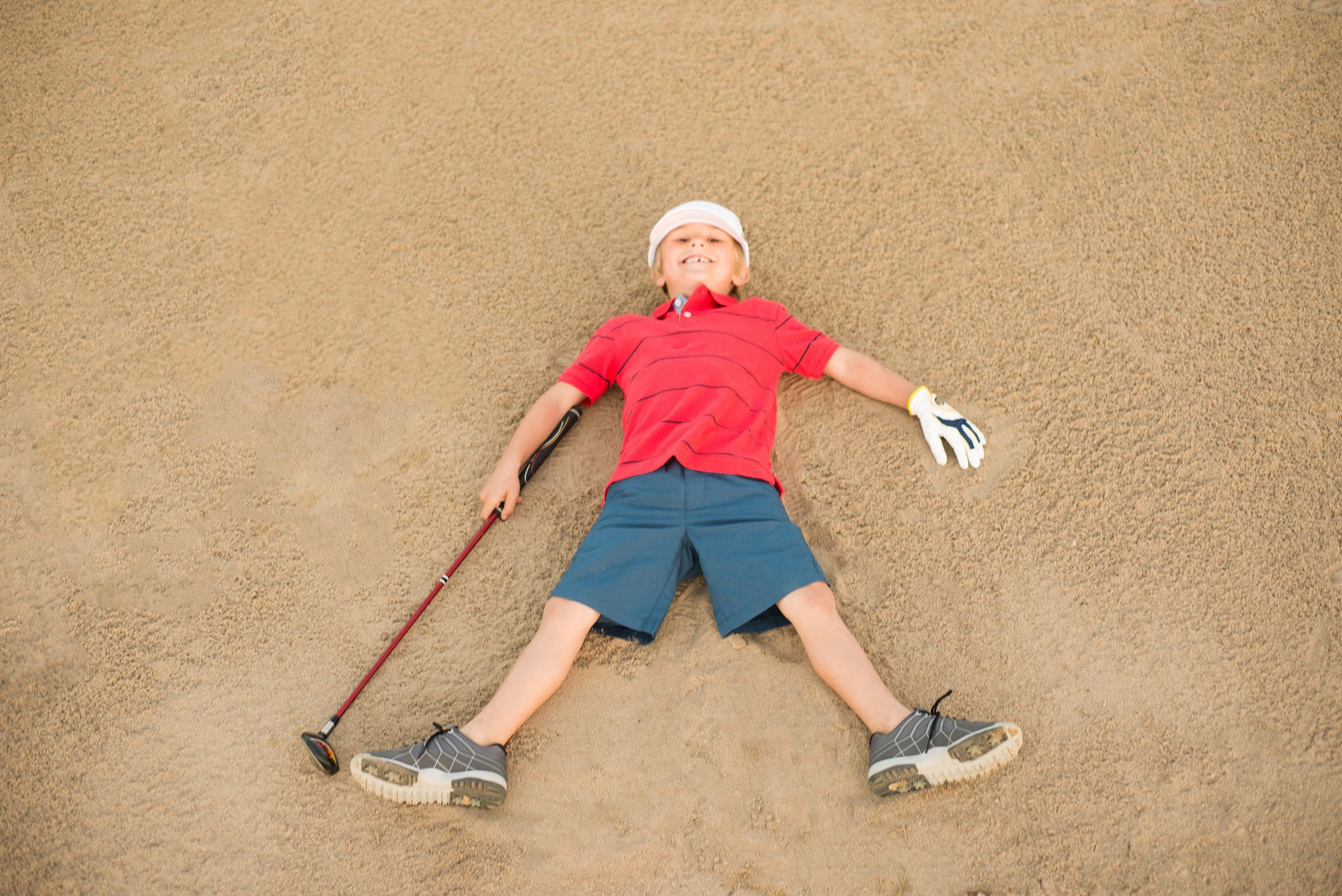 Young Boy Golfer Laying In A Sand Bunker Having Fun